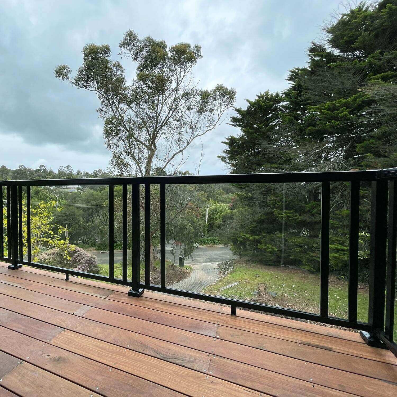 Wood balcony deck overlooking a driveway, featuring the black Peak Aluminium Balustrade system with a mix of glass panels and wide balusters.